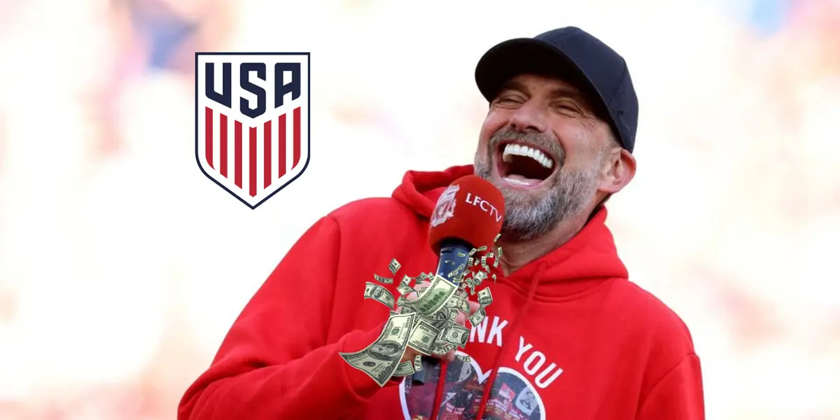 Jurgen Klopp laughs while he wears a special Liverpool sweater while the US National team badge is next to him and money is below him. (Source: The Irish Independent)