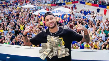 Neymar poses for a picture with hundreds of fans behind him and a stack of money in front of him. (Source: Team Ney 10 X)